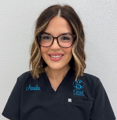 Aarika, Clinical Assistant at Graf Orthodontics, smiling in black scrubs with embroidered name and logo, showcasing expertise and friendly demeanor.